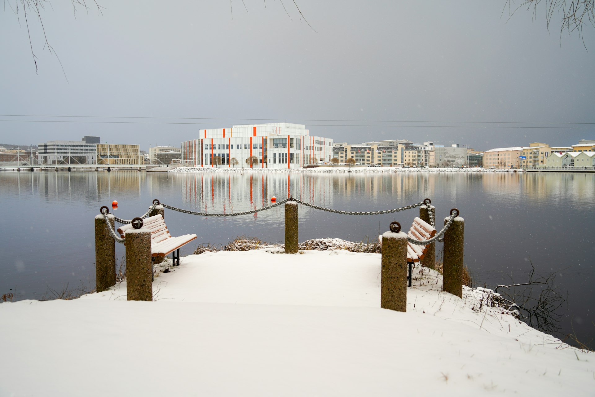 A snow covered pier with benches and a building in the background