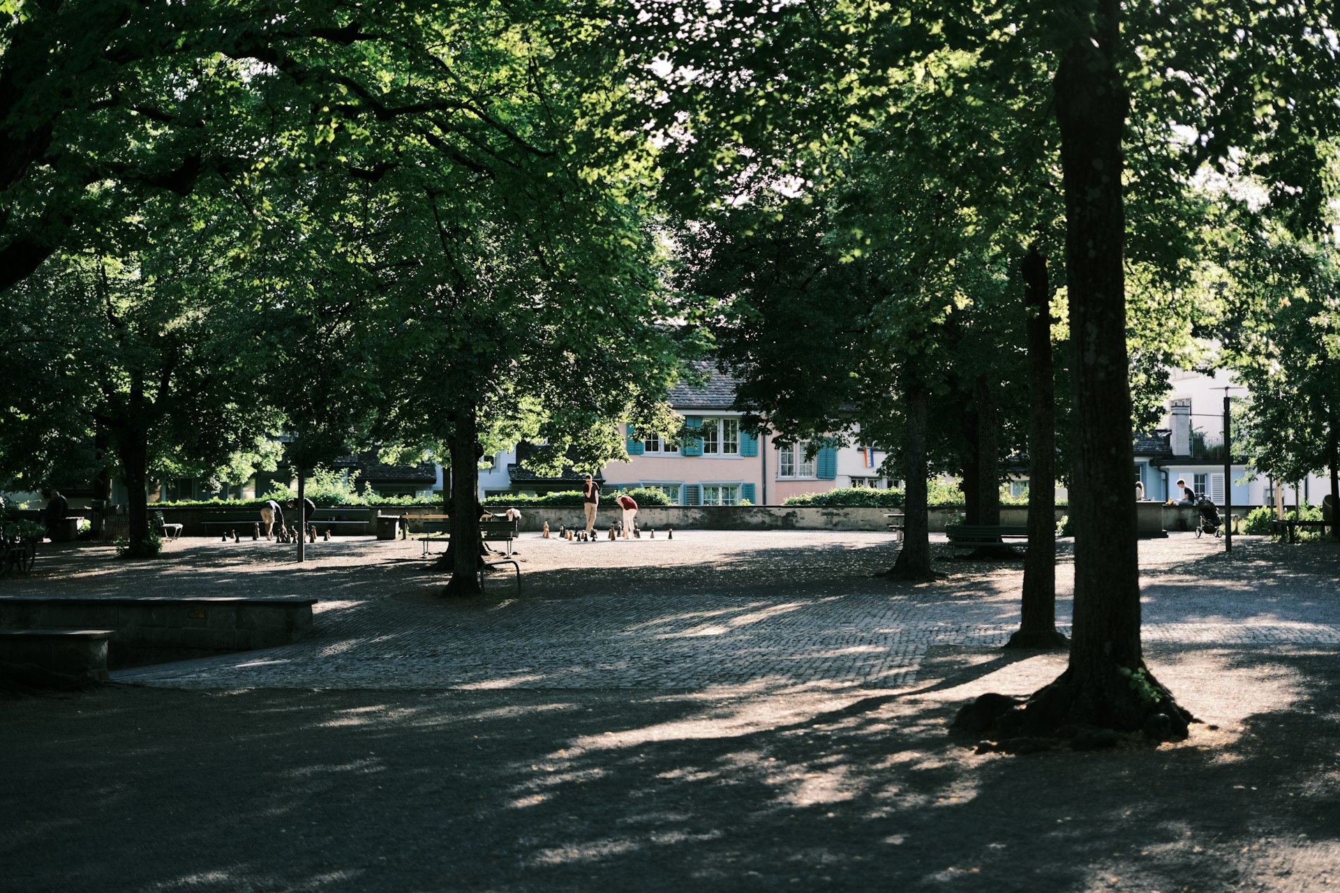 a park with benches, trees, and a building in the background