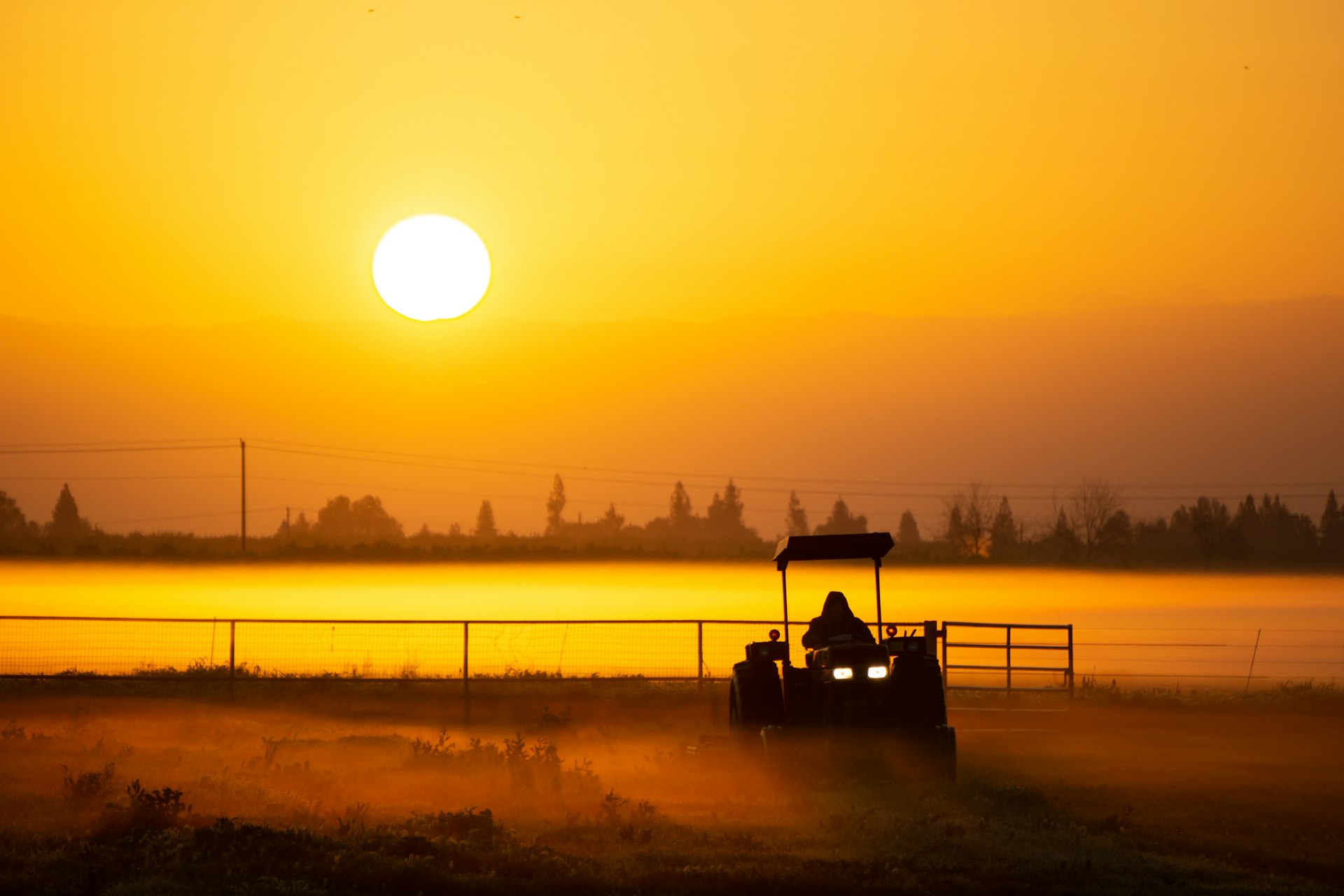 a person driving a tractor in a field at sunset