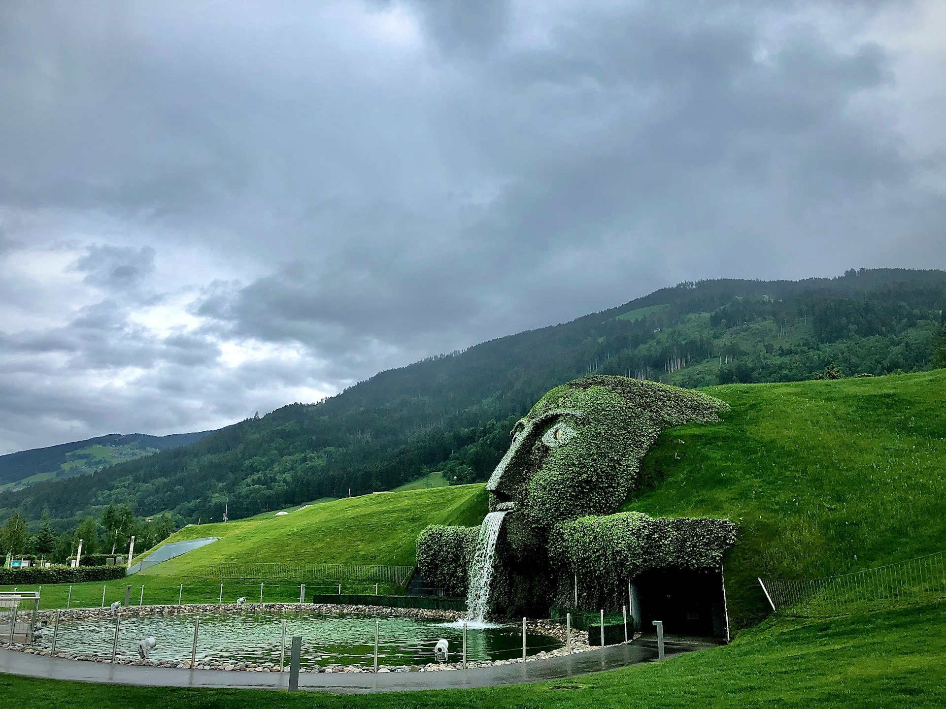 green grass field near green mountain under white clouds during daytime