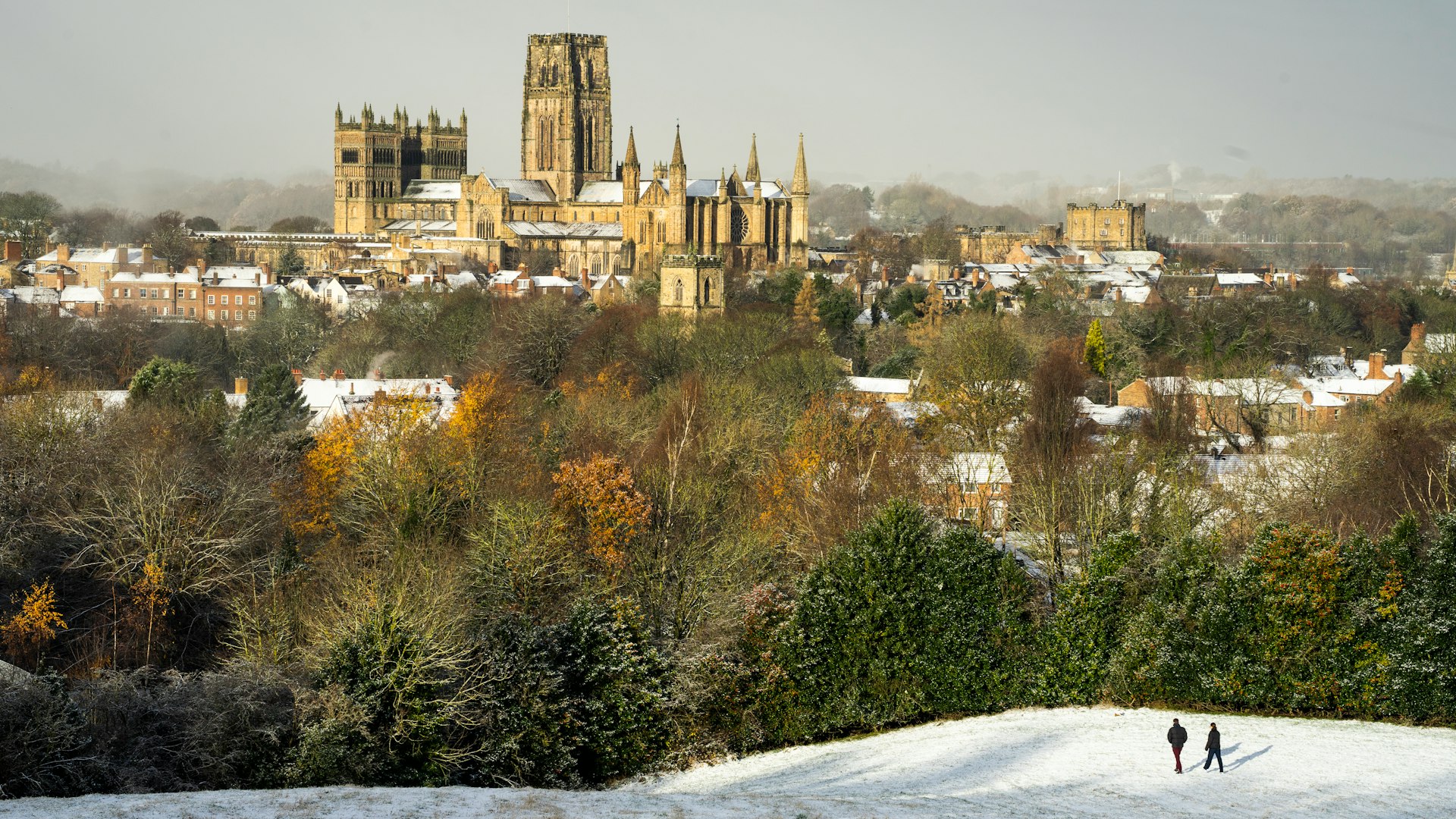 two people walking in the snow in front of a city