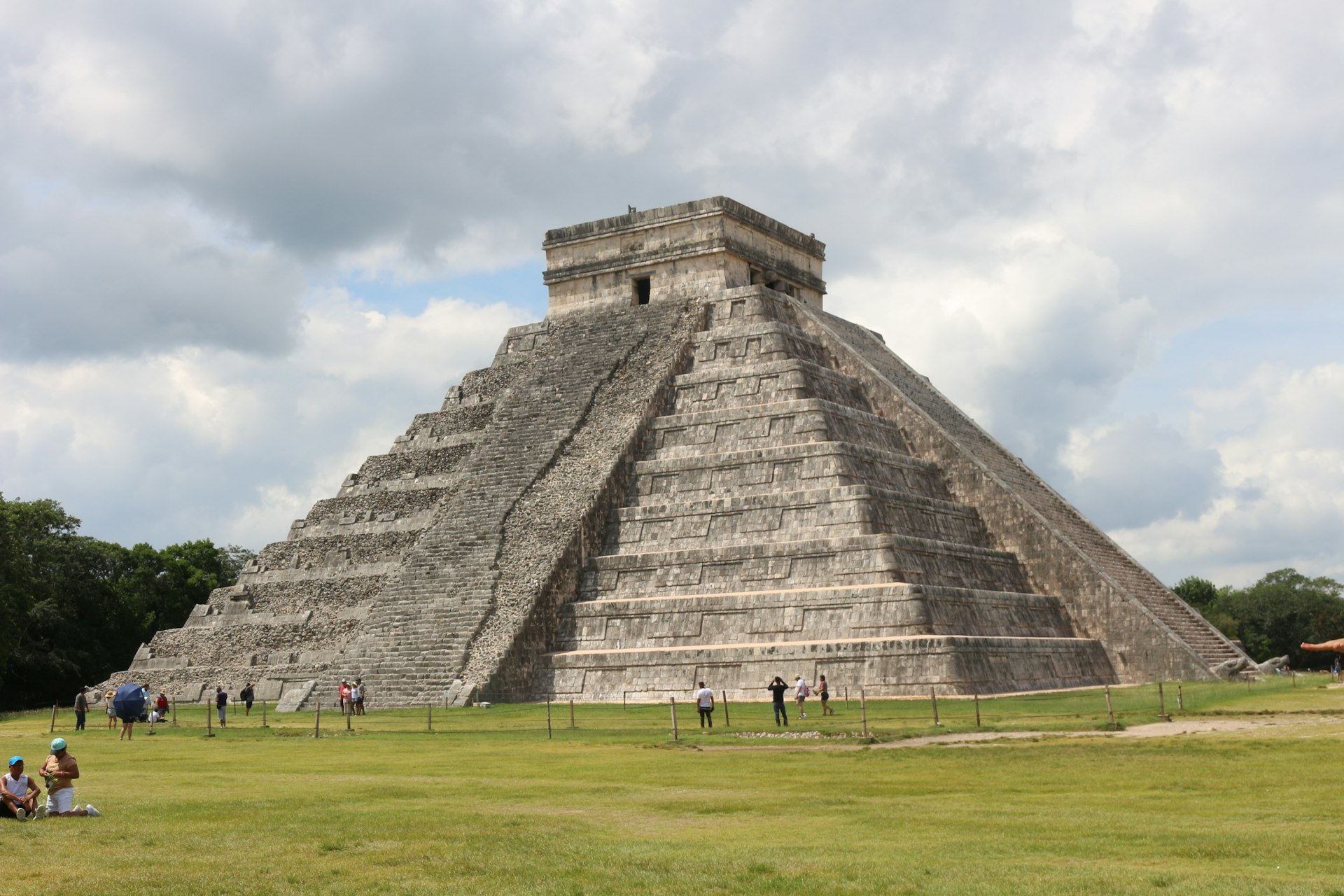 a pyramid with people standing around with Chichen Itza in the background
