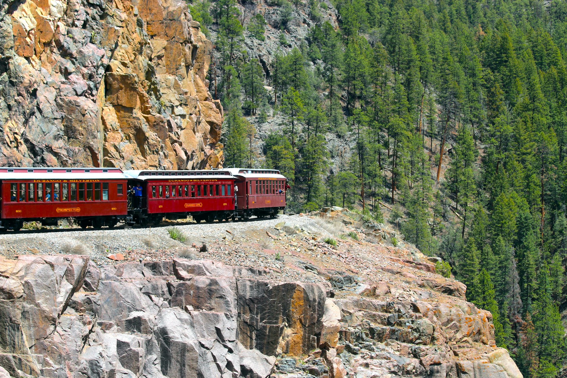 a red train traveling down train tracks next to a mountain