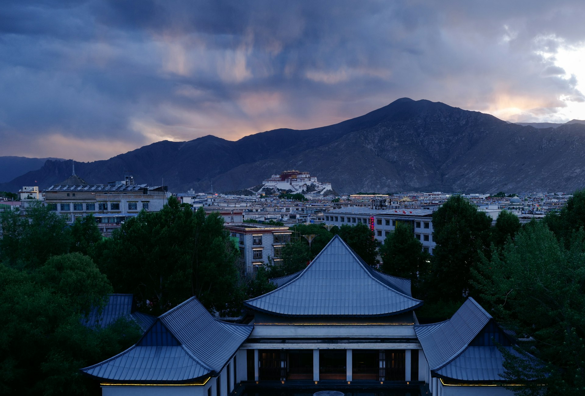 white and blue house near green trees and mountain under cloudy sky during daytime