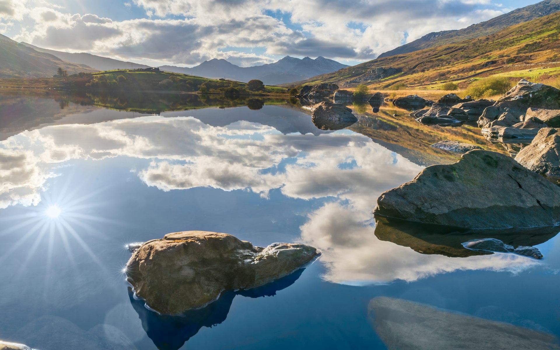 brown and green mountain beside lake under white clouds and blue sky during daytime